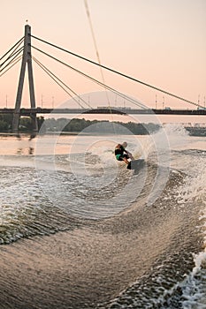 strong adult man holds rope and energetically balancing wakeboard on splashing river water