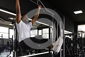 Strong african man doing statics exercise on horizontal bar, having workout at gym. photo