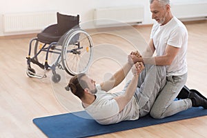 Strong aged orthopedist assisting the disabled in the gym