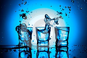 Strong alcoholic drink in dammed glasses with splashes on a blue background