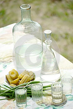 Strong alcoholic homemade drink moonshine in glass vintage containers and pickled cucumbers. Traditional rural still life of Ukrai