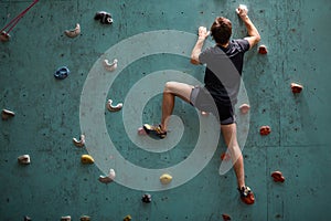 Strong anf git young caucasian man on rock wall in sport center, rock climbing
