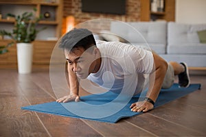 Strong asian mature man making strength workout, doing push ups on sports mat, having domestic workout