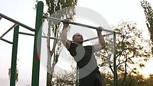 Strong athlete in black sportclothes doing pull-up on horizontal bar. Mans fitness with blue sky and trees in the