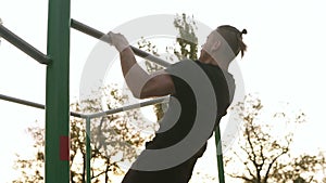 Strong athlete in black sportclothes starting doing pull-up on horizontal bar. Man exercising outdoors. Trees in the