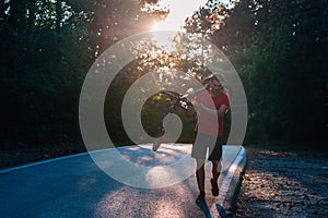 Strong athlete cyclist  biker  carrying his bicycle on his back on an asphalt road through deep green woods at sunset. Flat tire