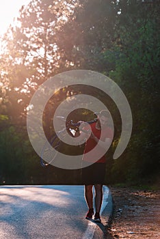 Strong athlete cyclist  biker  carrying his bicycle on his back on an asphalt road through deep green woods at sunset. Flat tire