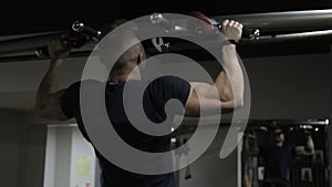 Strong athlete is pulled up on crossbar in sports club indoors.