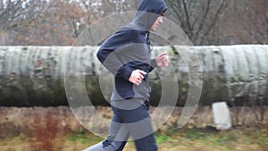 Strong athlete in sportswear jogging along trail at cloudy day. Young sportsman running along asphalt road in rain