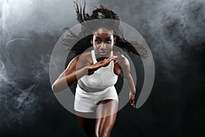 Strong athletic black skin woman sprinter, running on background with smoke wearing in the sportswear. Fitness and sport