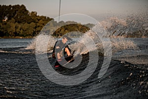 Strong athletic male wakeboarder holds rope and energetically riding wakeboard on splashing river water.