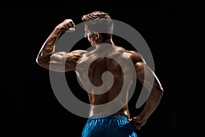 Strong Athletic Man Fitness Model posing back muscles, triceps over black background