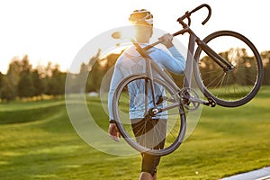 Strong athletic man in sportswear carrying his bicycle and watching amazing sunset after cycling in park