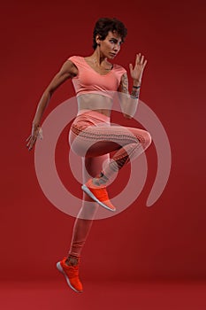 A strong athletic, woman sprinter or runner, running on red background wearing sportswear. Fitness and sport motivation.