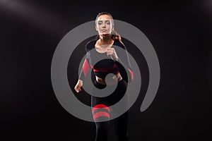 Strong athletic woman sprinter, running on black background wearing in the sportswear. Fitness and sport motivation