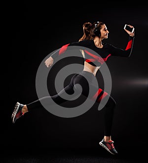 Strong athletic woman sprinter, running on black background wearing in the sportswear and headphones. Fitness and sport