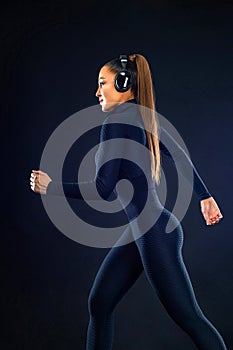 Strong athletic woman sprinter, running on black background wearing in the sportswear and headphones. Fitness and sport