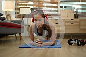 Strong athletic woman with wireless headphone doing plank exercise on matin living room photo