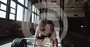 Strong athletic young bearded Caucasian man lifting heavy barbell in large hardcore gym hall. Power and strength concept