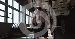 Strong athletic young bearded Caucasian man lifting heavy barbell in large hardcore gym hall. Power and strength concept