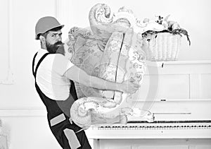 Strong bearded guy carrying old armchair alone. Mover in orange helmet isolated on white background