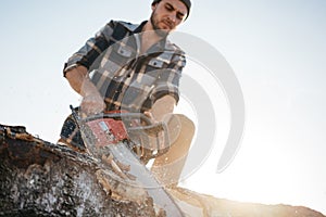 Strong bearded logger sawing a tree with chainsaw photo