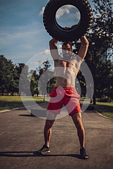 Strong bearded man holding tire overhead in the park