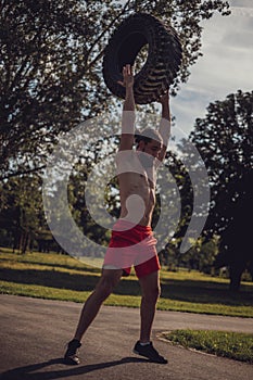 Strong bearded man holding tire overhead in the park