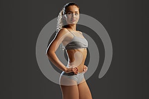 Strong and Beautiful. Beautiful young woman in underwear showing her perfect, fit, healthy body shape against grey photo