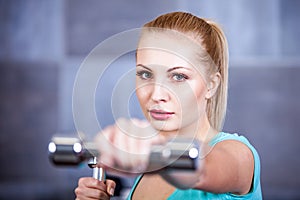 Strong blonde woman weightlifting at the gym, doing shoulders exercise