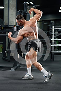 Strong bodybuilder demonstrating muscular body in sports gym.