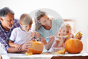 Strong bonds and special traditions. A family of four hollowing out pumpkins for halloween in the kitchen.