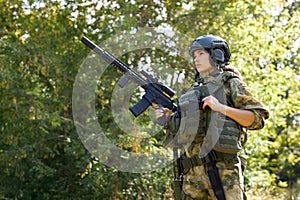 Strong brave female army soldier with rifle machine gun standing in the forest