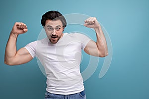 strong brunette young man in white t-shirt with biceps on studio background with copyspace