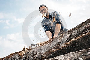 Strong and brutal lumberjack with ax in his hands chops tree in forest, wood chips fly apart