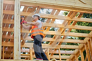 Strong builder standing on wooden building, putting gilder, holding hammer, beating.