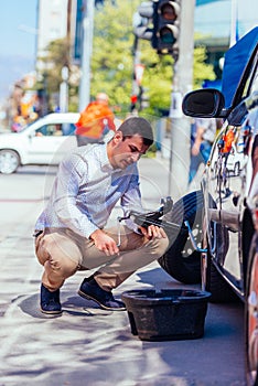 A strong businessman is bending his knee while trying to change a flattie on his car with his lug wrench