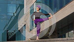 Strong calm woman muslim islamic girl in hijab barefoot lady in purple pants stands city building background bending