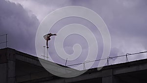 Strong circus Artist keep balance by one hand on the edge of rooftop against amazing cloudscape. Risk, courage and