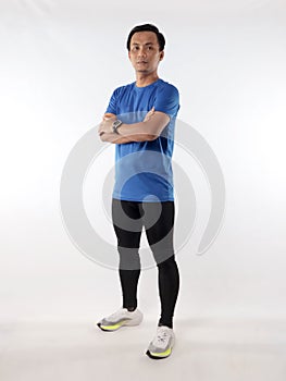 Strong confidence athletic young Asian male wearing running jersey looking at camera with crossed arms, full length studio shot