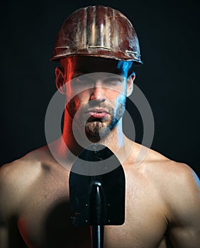 Strong construction worker with nude torso in safety hardhat with spade. Serious bearded man in hard hat with shovel in