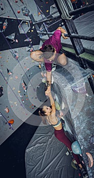 A strong couple of climbers climb an artificial wall with colorful grips and ropes.