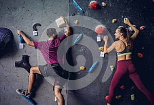 A strong couple of climbers climb an artificial wall with colorful grips and ropes.