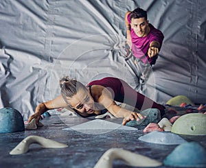 A strong couple of climbers climb an artificial wall with colorful grips and ropes.
