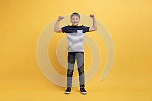 Strong cute kid boy showing muscles, yellow background