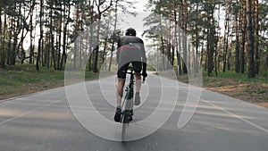 Strong cyclist riding a bicycle out of the saddle. Cyclist with strong leg muscles pedaling. Back follow shot. Cycling concept.