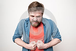 Strong, embittered bearded man clenched his fists and looks furiously at the camera, on a white background