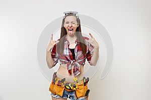 Strong excited handyman woman in plaid top shirt, denim shorts, kit tools belt full of instruments in protective goggles