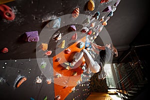 Strong female climber on boulder climbing wall indoor