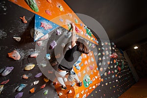 Strong female climber on boulder climbing wall indoor